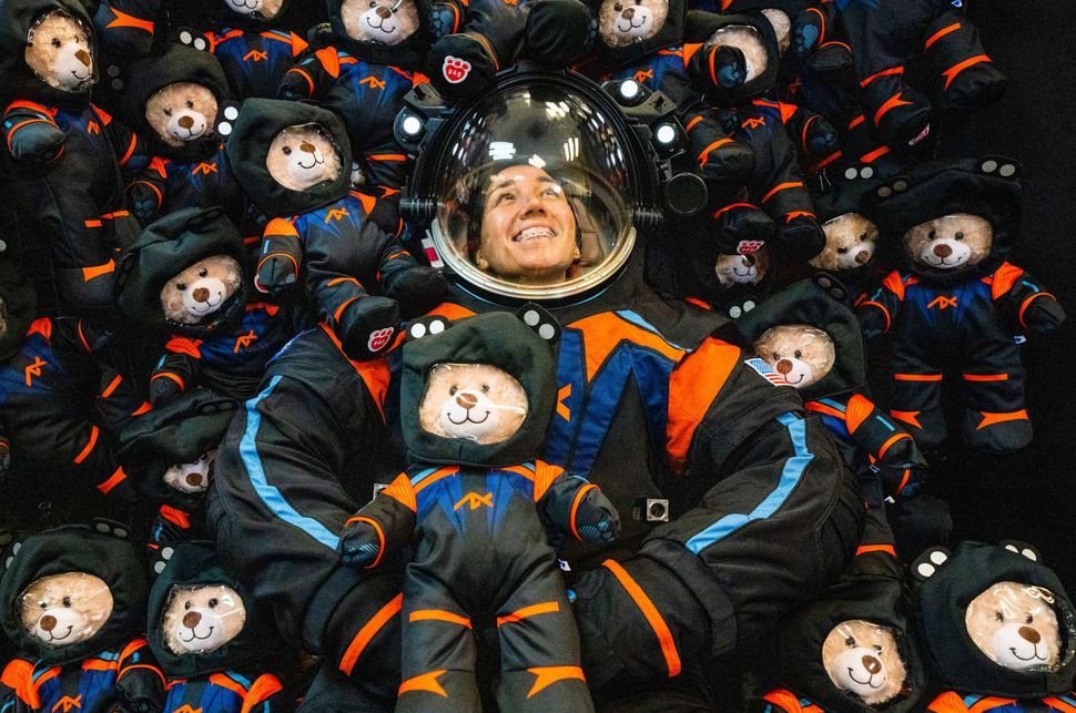 Um representante da Axiom Space usa o traje espacial AxEMU da empresa enquanto “nada” em um mar de bonecos Build-A-Bear “Happy Hugs Teddy”, cada um vestido com uma réplica da roupa de pressão lunar da próxima geração.