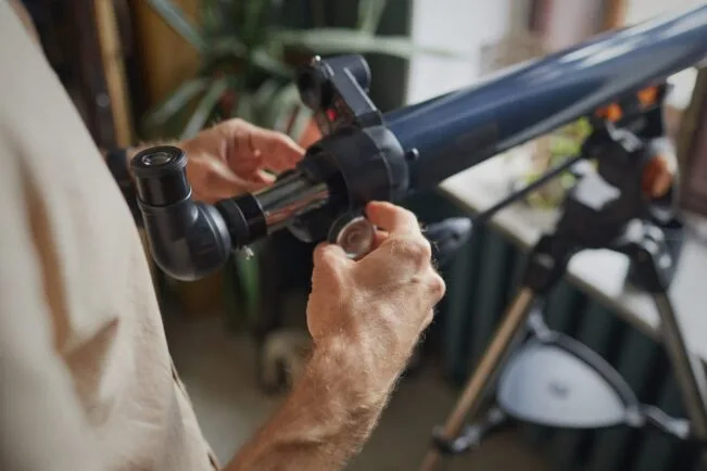 Homem usa telescopio enquanto o segura com suas duas mãos