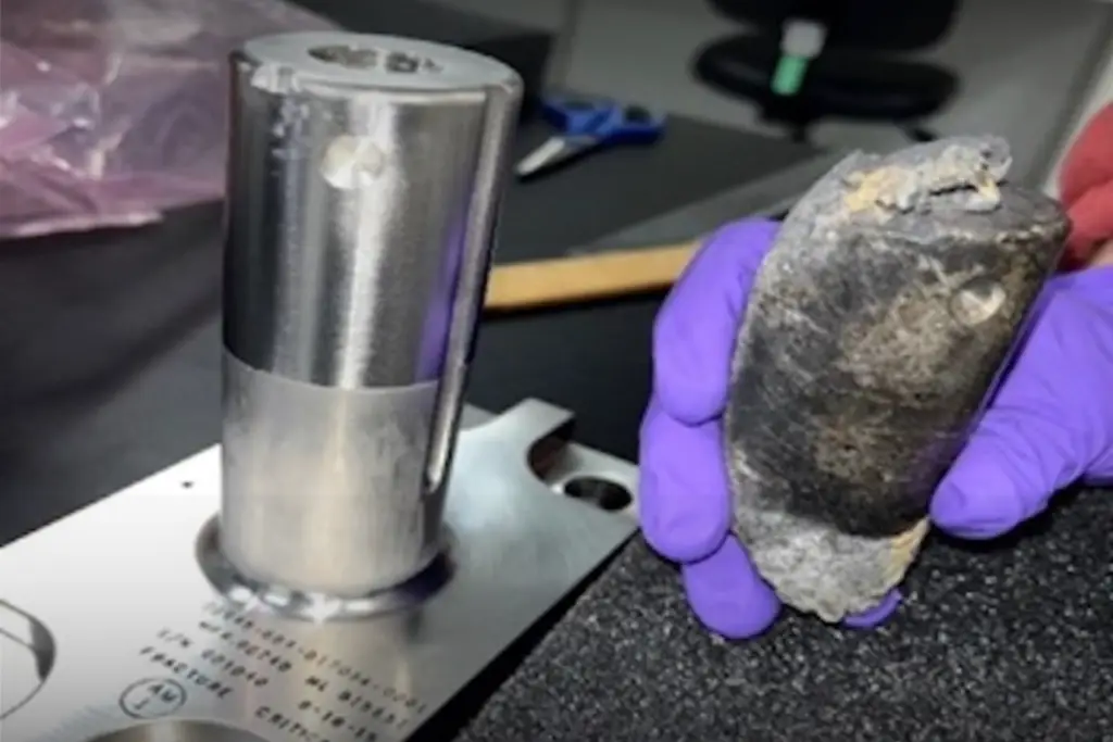 pedaço de 720 gramas de lixo espacial na cor cinza segurado por mãos humanas com luva de borracha na cor azul