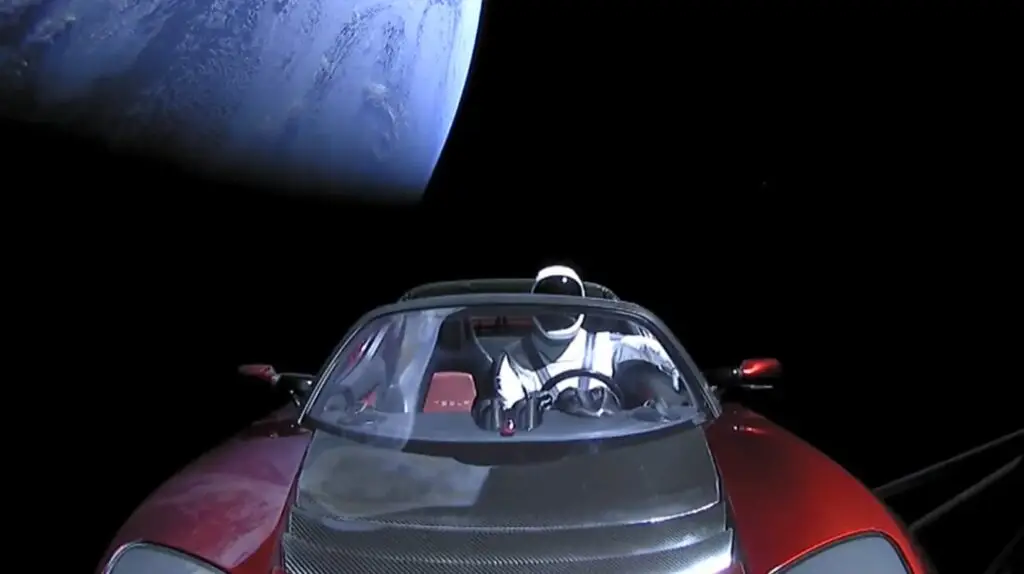 Carro Tesla Roadster vermelho com o manequim Starman orbitando o espaço com a terra vista ao fundo.