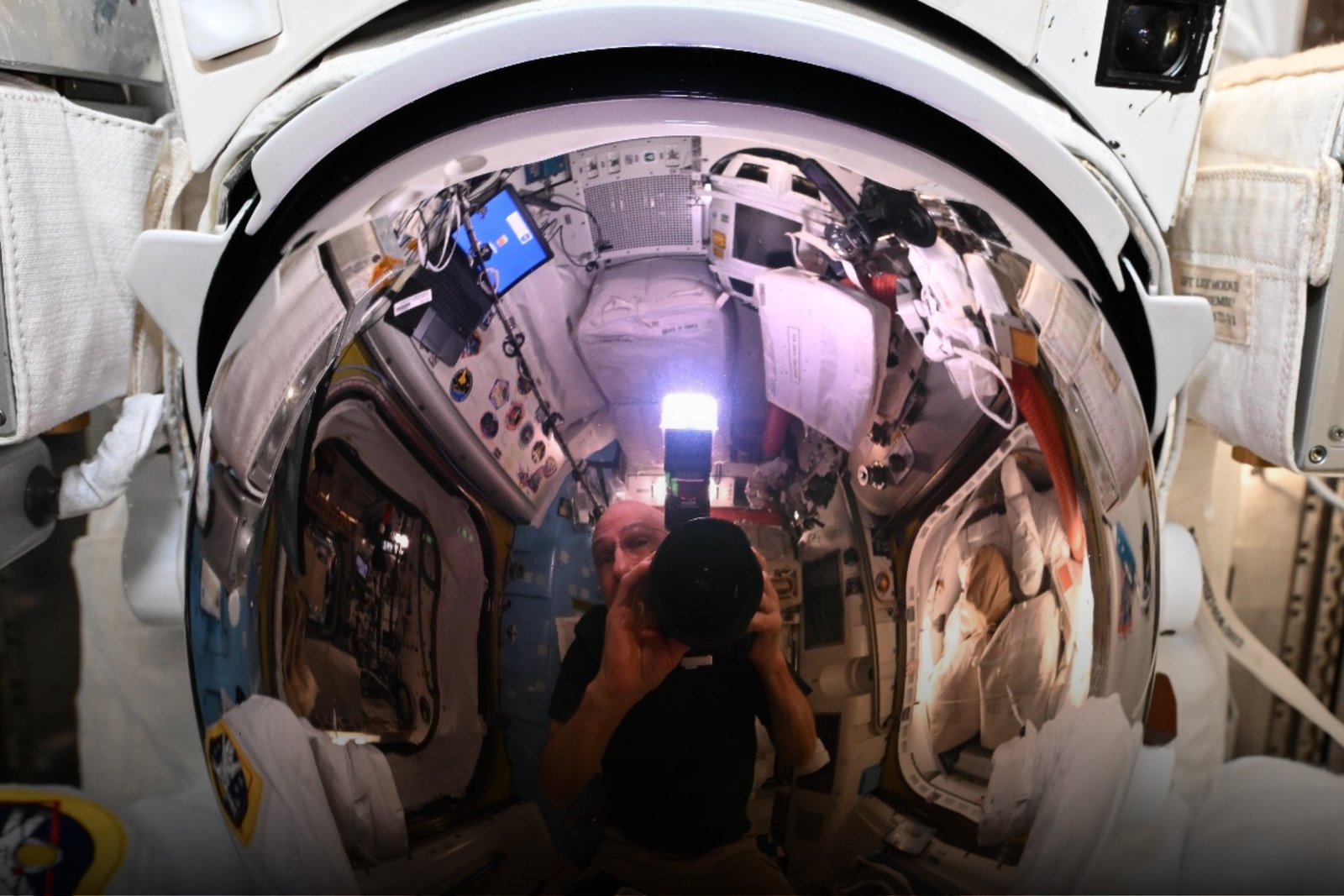 Reflexo no visor do capacete de um traje espacial mostrando o interior da Estação Espacial Internacional (ISS). A imagem destaca os equipamentos, a microgravidade e a vida a bordo, ilustrando como os astronautas sobrevivem no espaço