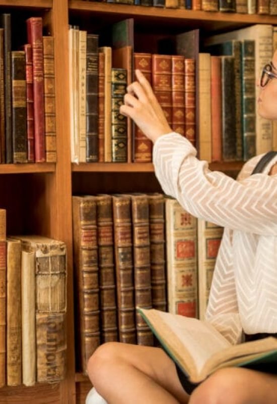 menina sentada pegando livros de ficção científica em uma estante